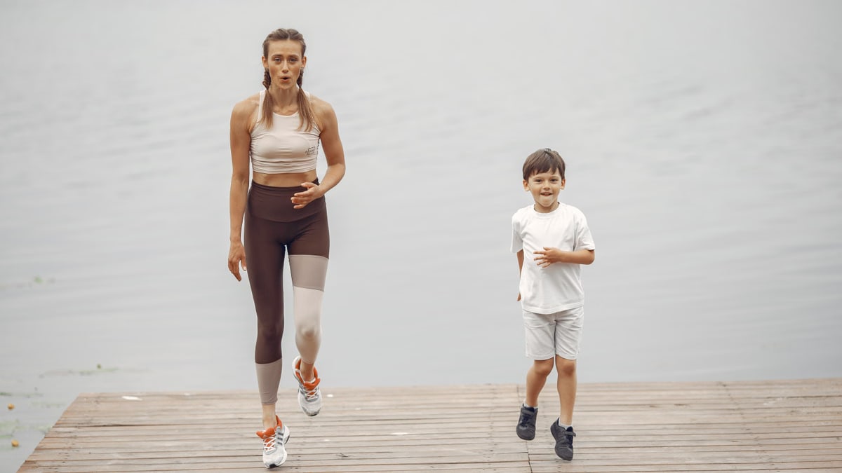 A woman and young boy jogging together on a wooden pier by a tranquil lake, enjoying leisure time outdoors.